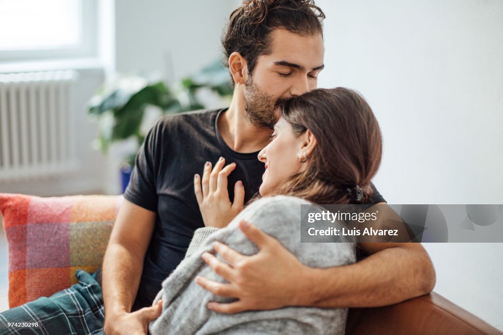 Man embracing girlfriend while kissing on her forehead at home