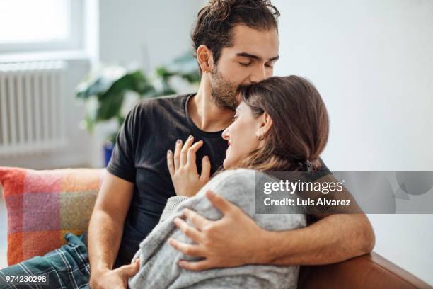 man embracing girlfriend while kissing on her forehead at home - casal heterossexual imagens e fotografias de stock