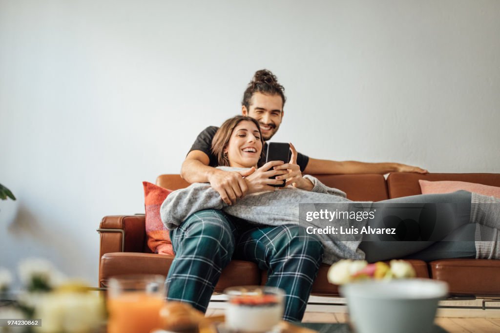 Young couple with smart phone relaxing on sofa
