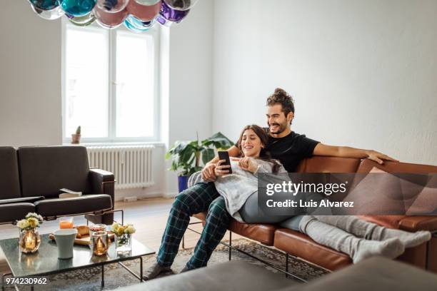 young couple using mobile phone on sofa at home - mann ganzkörper casual stock-fotos und bilder