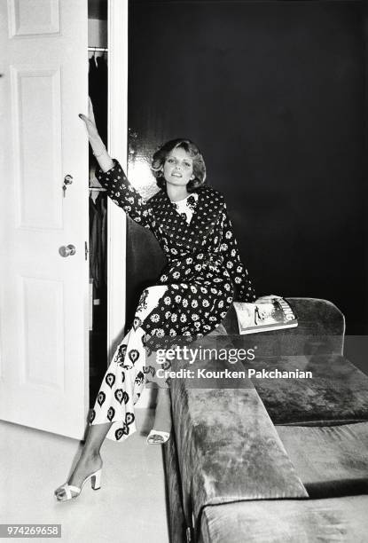 Model Cheryl Tiegs, sitting on back of a couch, wearing a quilted challis robe in a foulard print over a reverse-print tricot pajama by Donald Brooks.