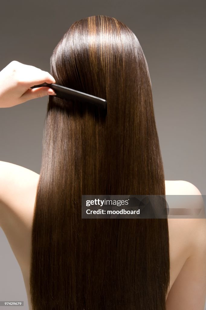 Woman combing long brown hair, rear view