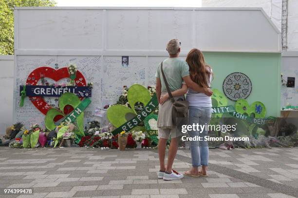 Couple look at tributes left at a memorial wall by Grenfell Tower on the one year anniversary of the Grenfell Tower fire on June 14, 2018 in London,...