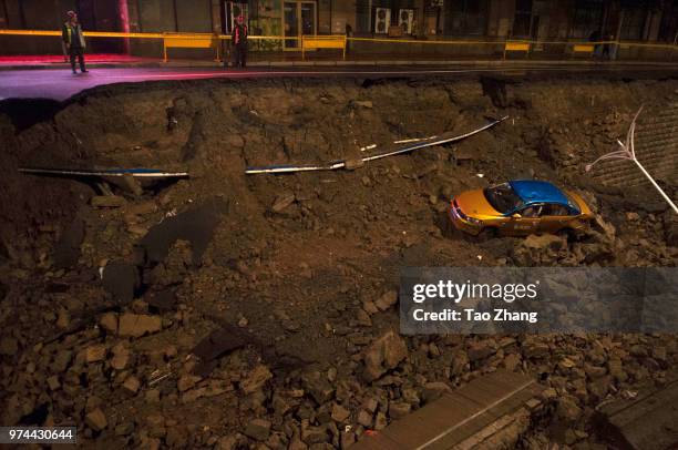 Taxi is shown having fallen to a lower roadway after a heavy rainstorm caused a wall collapse on a city street on June 14, 2018 in Harbin, China. Two...