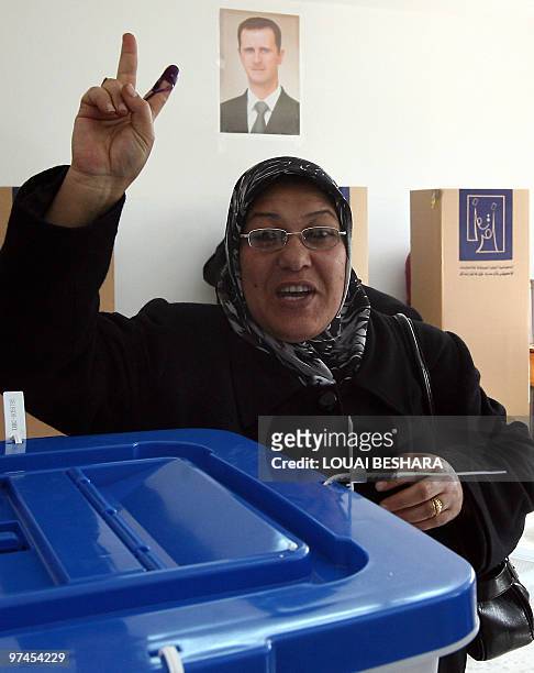 Under a portrait of Syrian President Bashar al-Assad an Iraqi refugee woman flashes the V for "victory" sign after casting her ballot a a polling...