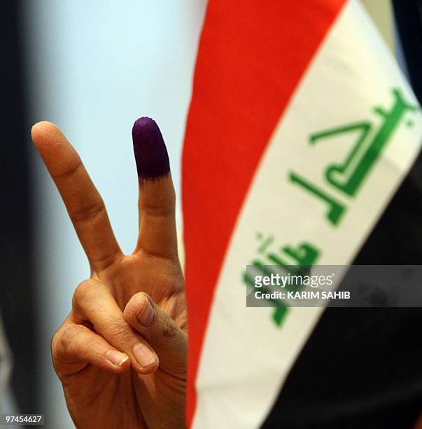An Iraqi expatriate flashes the victory sign with his ink-stained finger in front of his national flag after casting his vote for the Iraqi general...