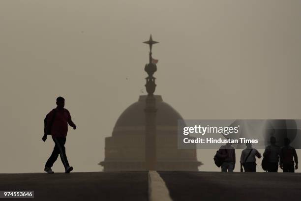 People cross the road as Rastrapati Bhavan is seen in the backdrop engulfed with haze, at Rajpath, on June 14, 2018 in New Delhi, India. Many areas...