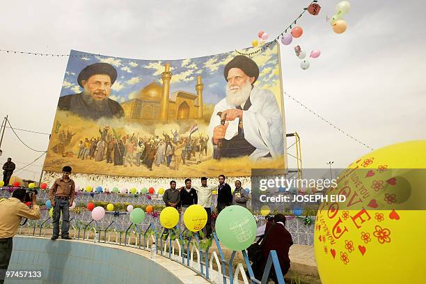 Iraqi Shiite Muslims pose for pictures in front of a renovated mural bearing the pictures of Shiite clerics Mohammed Baqer al-Sadr and Mohammed Sadeq...