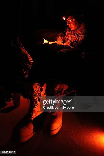 Army chaplain Carl Subler reads under the glow of his red-filtered head lamp as his combat boots stand near his cot early on March 5, 2010 at an...