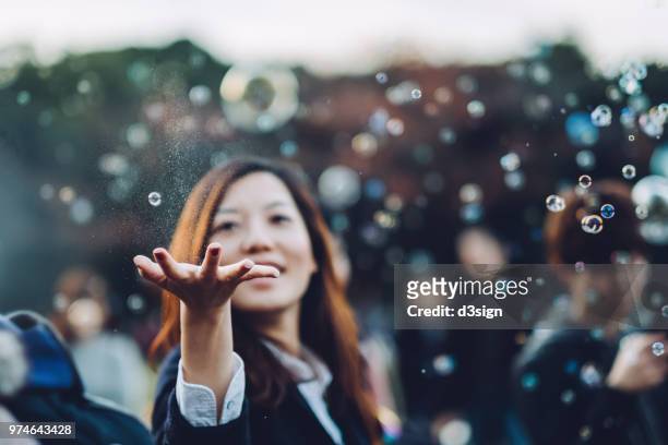 young woman catching bubbles joyfully in park - bubbles happy stock-fotos und bilder
