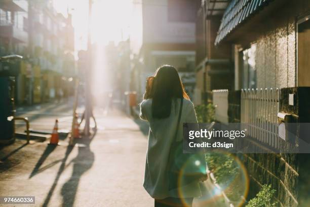 rear view of woman leaving home to work in the early morning against warm sunlight - marche ville photos et images de collection