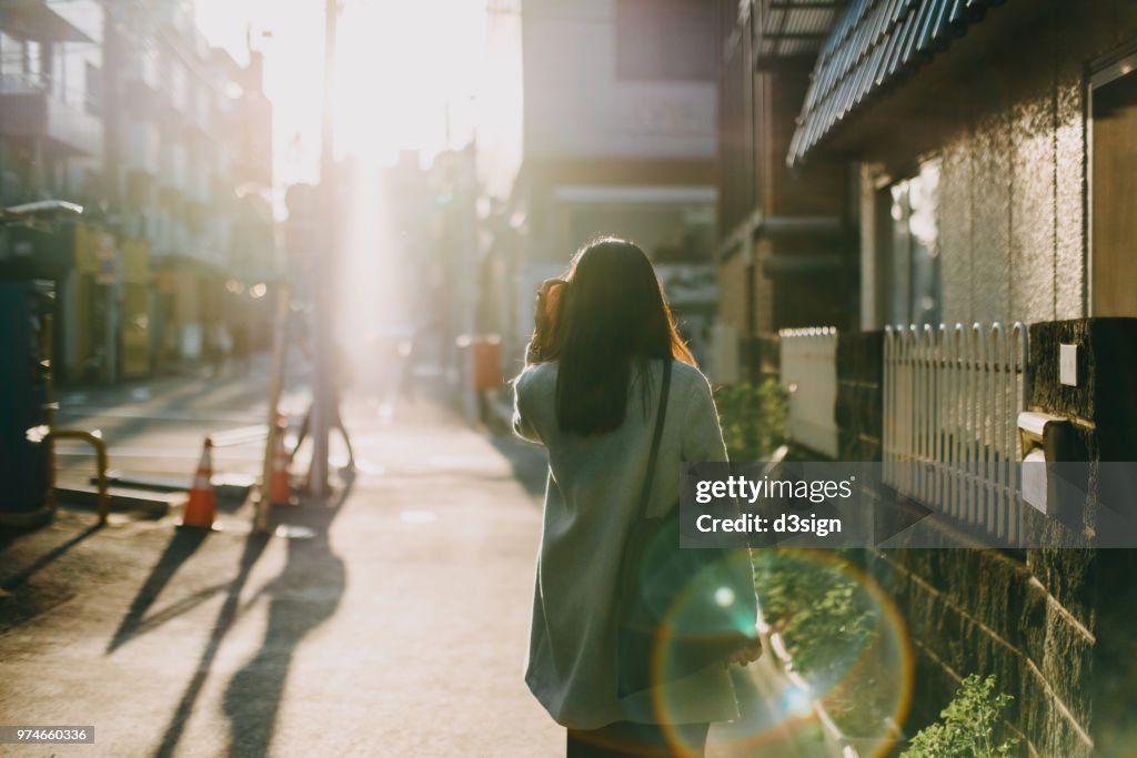 Rear view of woman leaving home to work in the early morning against warm sunlight