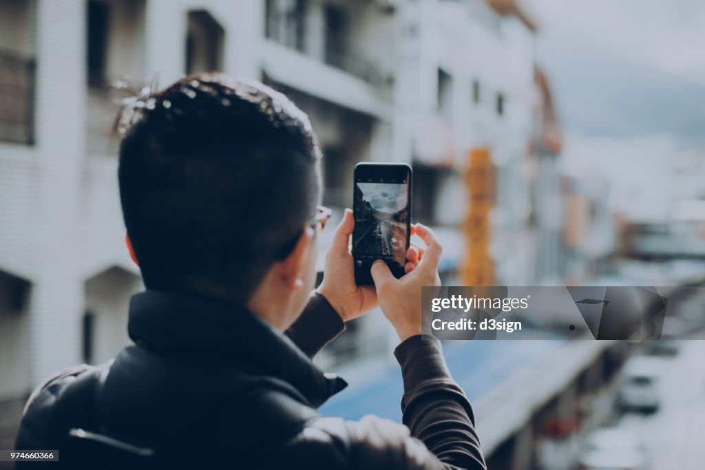 Close up of male traveller taking photo of Hakone street view with mobile phone on terrace