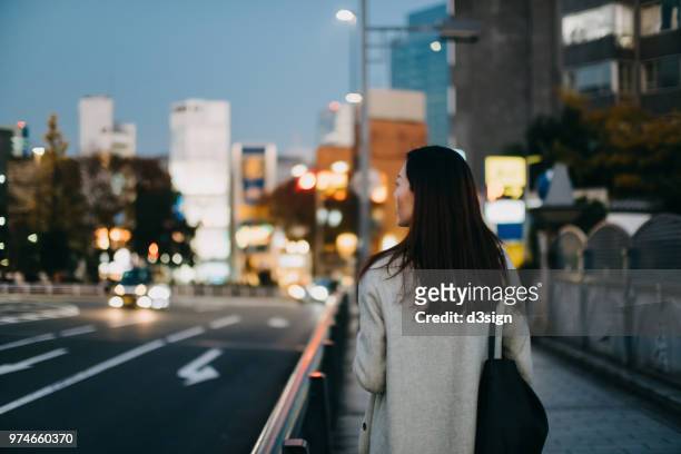 young woman waiting for a taxi ride in downtown city street at dusk - stile stock-fotos und bilder
