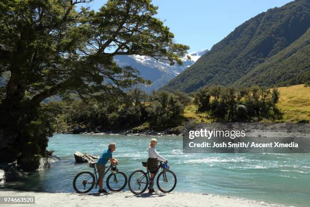 mountain bikers discover riverside beach, mountains distant - wanaka stockfoto's en -beelden