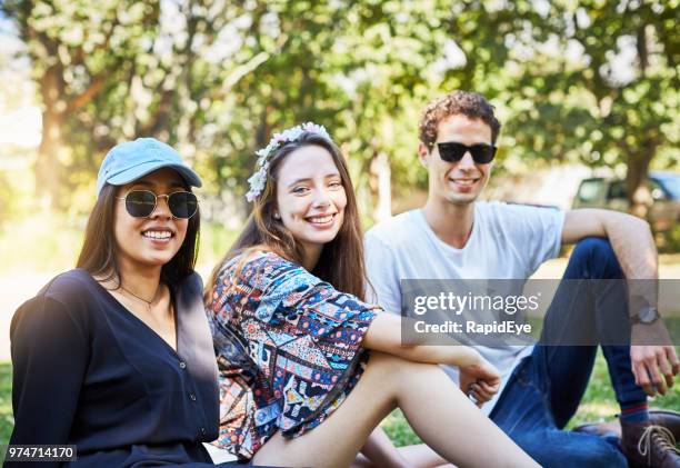 trois jeunes amis s’asseoir sur une ligne sur la pelouse du parc - small group sitting in grass photos et images de collection