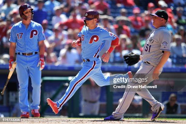 Andrew Knapp of the Philadelphia Phillies runs by Jake McGee of the Colorado Rockies to score on a passed ball as Rhys Hoskins looks on in the...