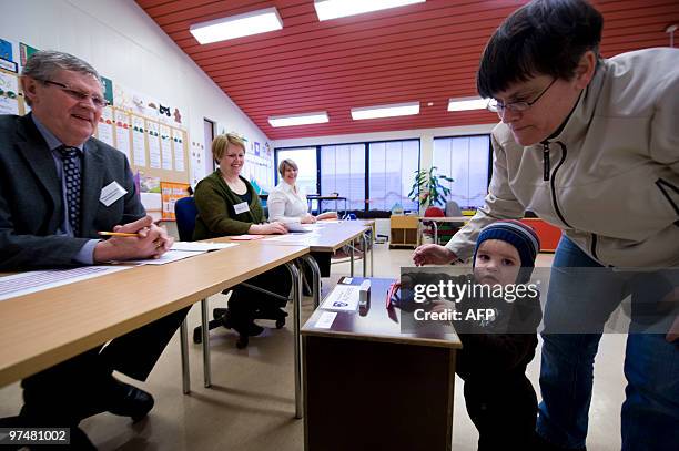 Electoral employees smile to a child standing by its mother casting her vote at the Alftanes polling station on March 6, 2010. Iceland polling...