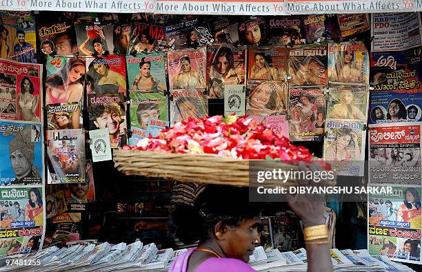 An Indian vendor carries a basket of flowers as she walks past a roadside newspaper and magazine stall in Bangalore on March 6, 2010. A bill...