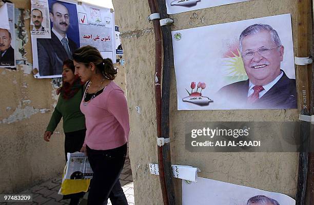 Iraqi Kurdish women walk past campaign posters for parliamentary candidates and President Jalal Talabani in the northern city of Sulaimaniyah on...