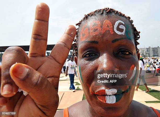 Female supporter, her face painted with the word "Gbagbo" and her lips and cheeks painted in the national colours, flashes the V-sign wears a...