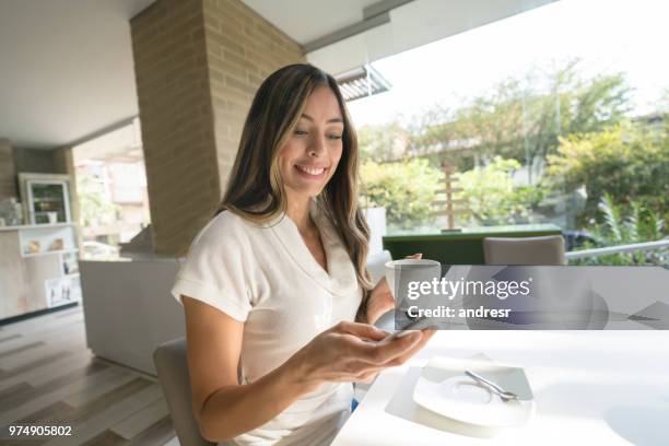 envoyer des sms sur son téléphone portable tout en ayant une tasse de café femme - sms'en photos et images de collection