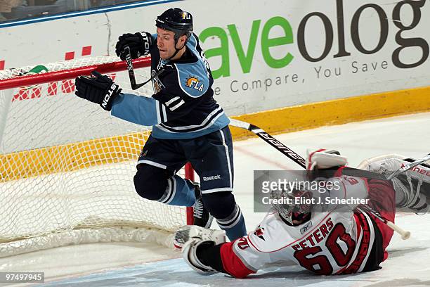 Gregory Campbell of the Florida Panthers dodges Goaltender Justin Peters of the Carolina Hurricanes at the BankAtlantic Center on March 6, 2010 in...