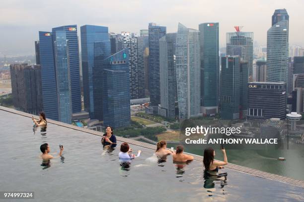 This photo taken on June 13, 2018 shows people using their phones to take photos in the rooftop pool of the Marina Bay Sands resort hotel, which...