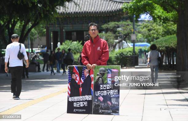 South Korean activist holds placards showing images of the Trump-Kim summit and a South Korea-US joint military drill during a rally to demand a halt...