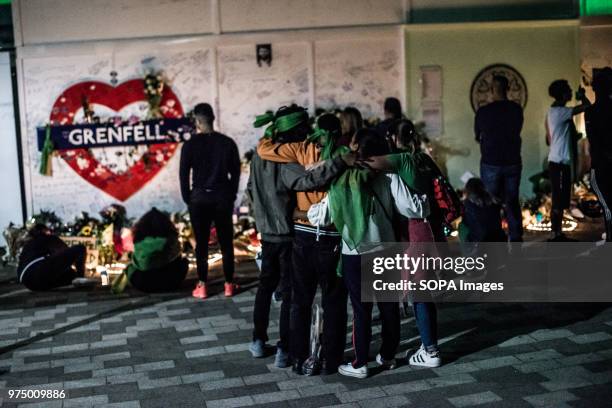 People seen embracing themselves at the foot of the Grenfell Tower before the flowers memorial. On the first anniversary of the Grenfell Tower fire,...