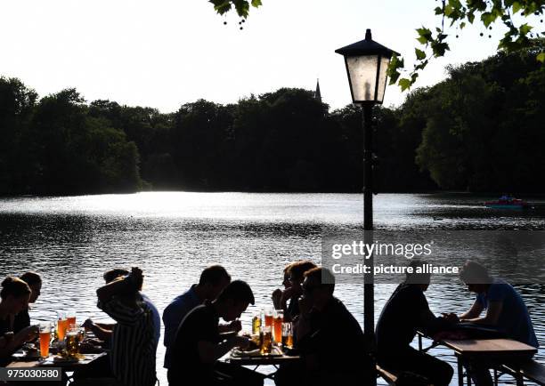 May 2018, Munich, Germany: Guests sit in the evening sun in the Seehouse bier garden on Kleinhesseloher See. People in Munich enjoy the beautiful...