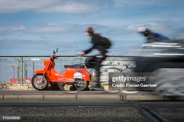 Two bikers and a car are pictured in front of an 'emmy' eScooter on June 14, 2018 in Berlin, Germany. Emmy is a sharing-based provider of electro...