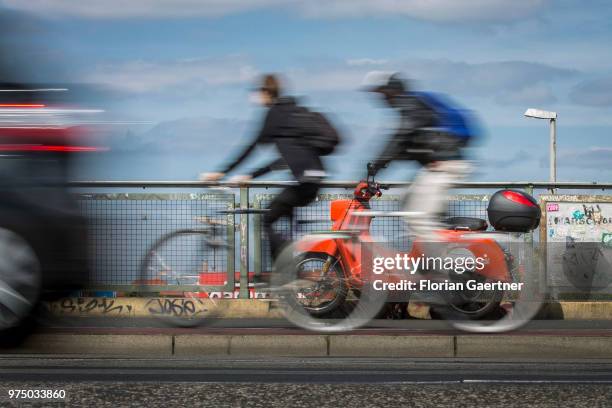 Two bikers and a car are pictured in front of an 'emmy' eScooter on June 14, 2018 in Berlin, Germany. Emmy is a sharing-based provider of electro...