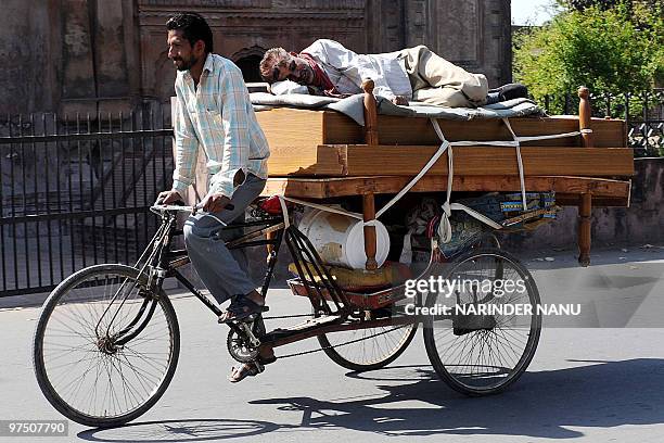Man takes a nap on a bed being transported by cycle rickshaw driver in Amritsar on March 7, 2010. These labourers earn approximately 100 rupees per...