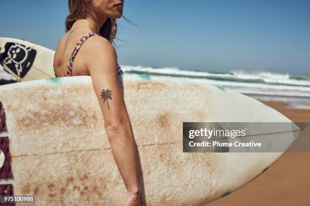woman holding surfboard on beach - tatuagem imagens e fotografias de stock