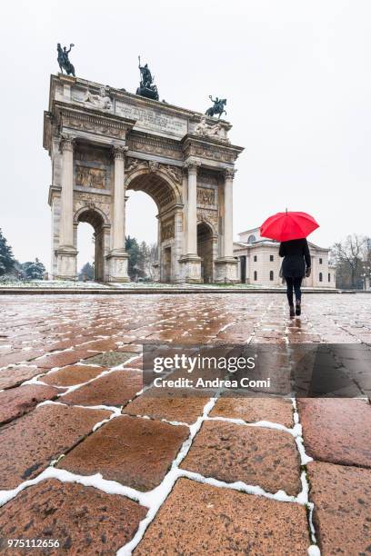 woman with red umbrella walks near the arch of peace during a snowfall. milan, lombardy, italy - andrea comi stock-fotos und bilder