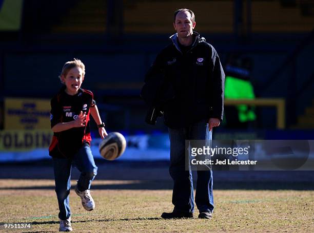 Saracens coach Brendan Venter watches his son play with a rugby ball on the pitch before the match during the Guinness Premiership match between...
