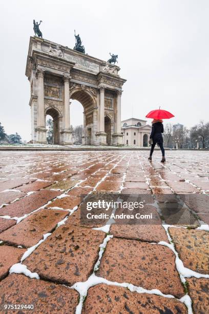 woman with red umbrella walks near the arch of peace during a snowfall. milan, lombardy, italy - andrea comi stock-fotos und bilder