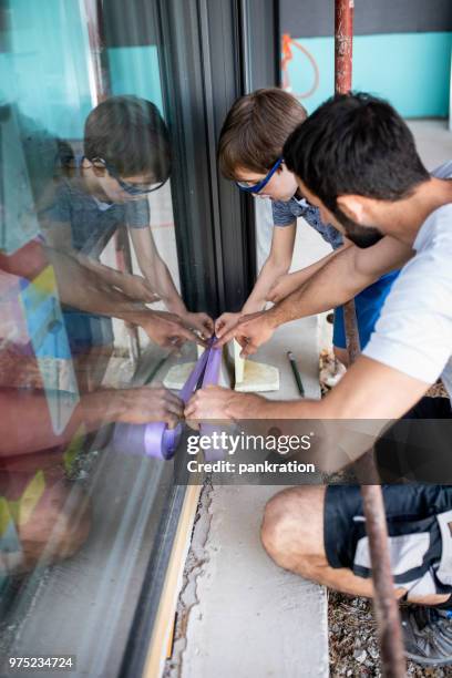 boy helping young man installing weather stripping on window - weather stripping stock pictures, royalty-free photos & images