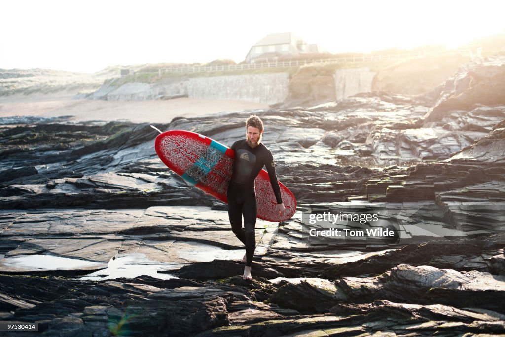 Male surfer walking across rocks with surfboard