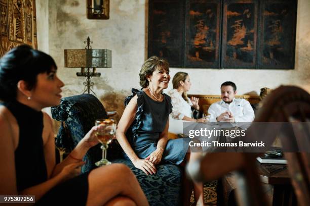 smiling grandmother sitting in living room with inlaws and children before dinner party - capital fotografías e imágenes de stock