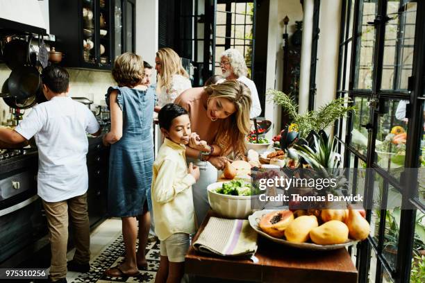 mother wiping sons face while preparing food in kitchen for family dinner party - kochen freunde stock-fotos und bilder