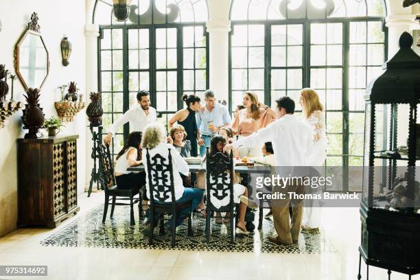 multigenerational family gathered around dining room table sharing food and drinks during party - wealthy family stock pictures, royalty-free photos & images
