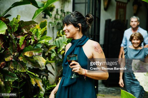 smiling woman holding drink walking into backyard during family dinner party - party dress stock-fotos und bilder
