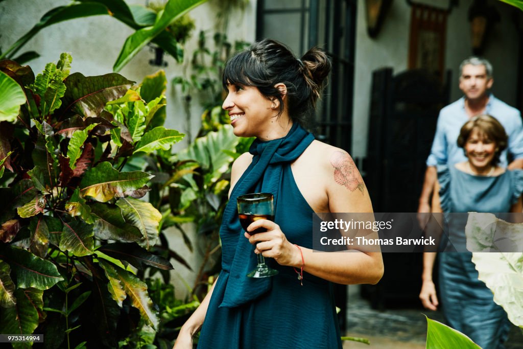 Smiling woman holding drink walking into backyard during family dinner party
