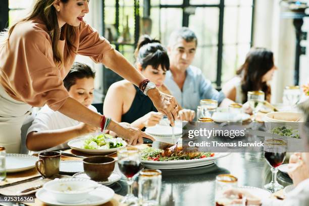 woman carving roast chicken at dining room table during family celebration meal - family at dining table stock pictures, royalty-free photos & images