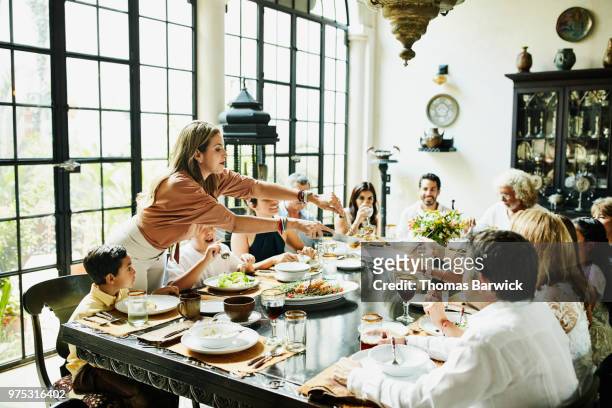 woman serving family members at dining room table during celebration meal - cena foto e immagini stock