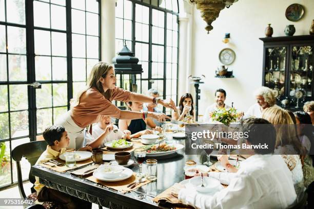 woman serving family members at dining room table during celebration meal - holiday table stock pictures, royalty-free photos & images