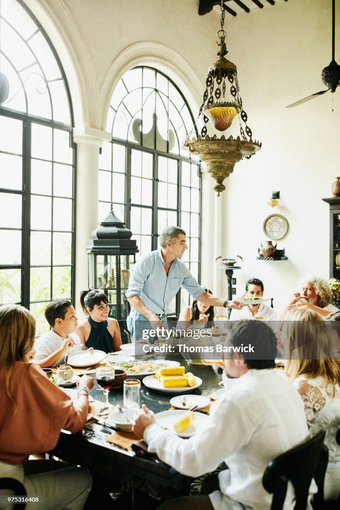 Man serving family members food at dining room table during family dinner