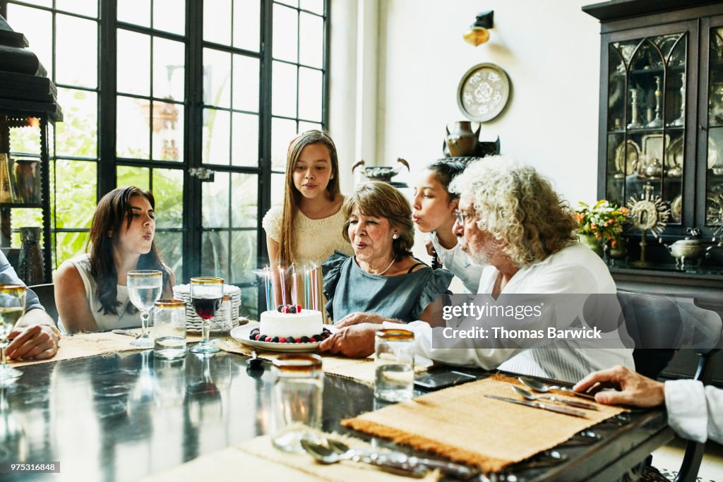 Grandmother and family blowing out candles on birthday cake during dinner party